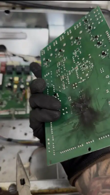 Back of a failed oven control board with a black burn mark, held by a technician